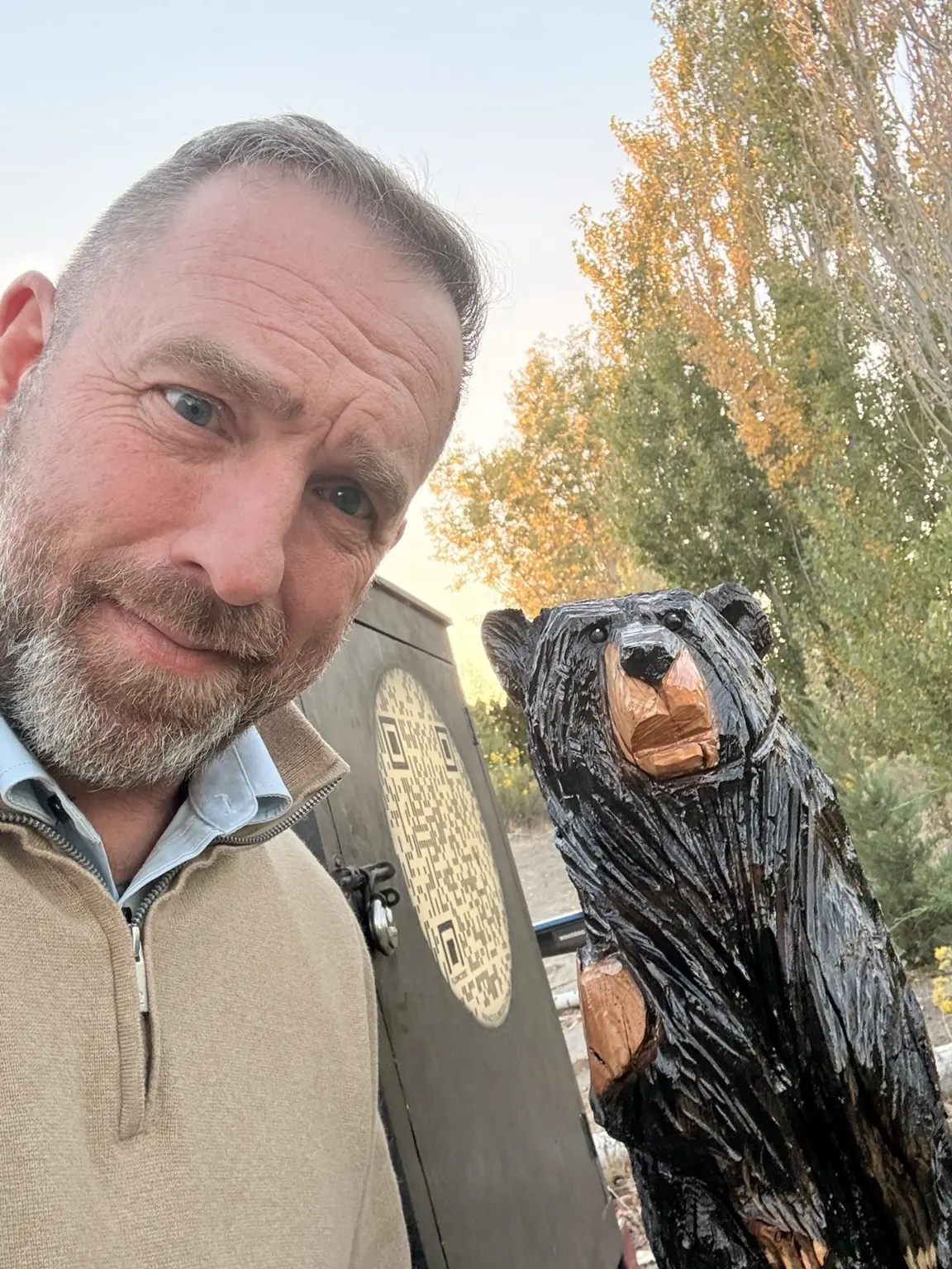 A man posing beside a glossy black bear chainsaw carving outdoors